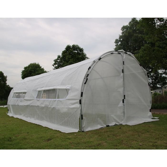 White greenhouse on grass under cloudy sky.